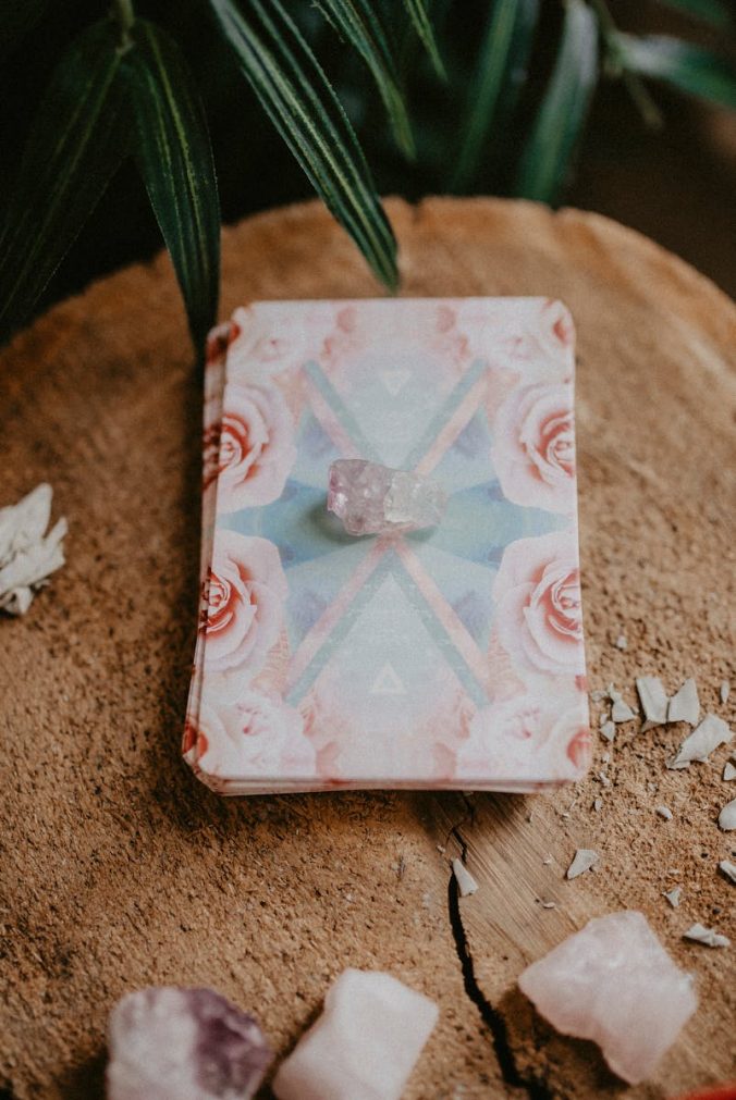 A healing crystal placed on floral tarot cards resting on chopped wood.