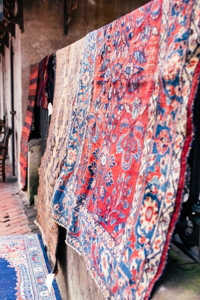 Colorful oriental carpets hang outdoors, showcasing intricate designs in a street setting.